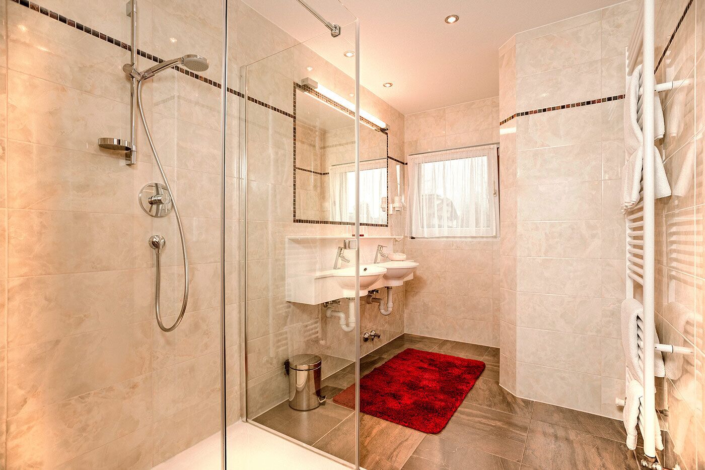 Une salle de bain moderne avec une douche à parois de verre, un meuble-lavabo doté de deux vasques et un tapis rouge sur le sol.
