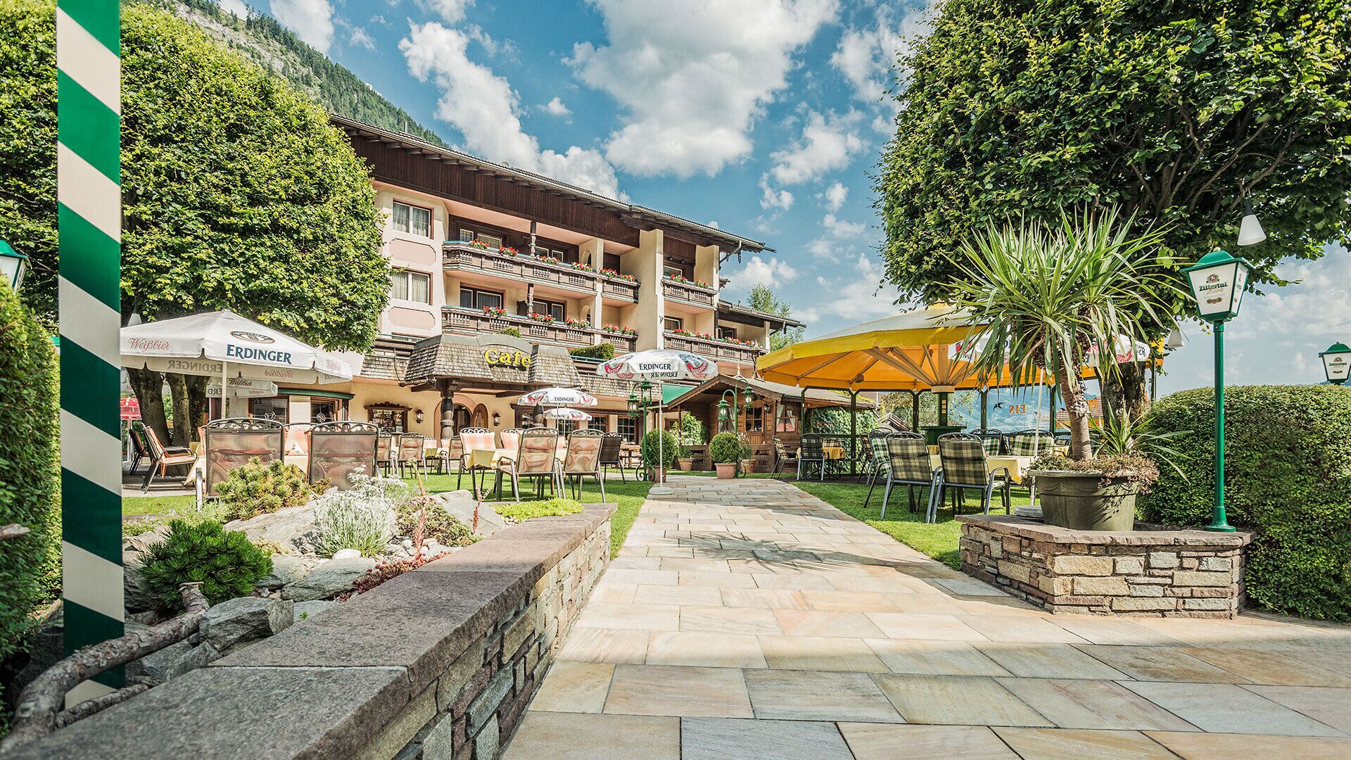 Ein Hotelinnenhof mit Außenbestuhlung, einem Café und einer Bergkulisse.