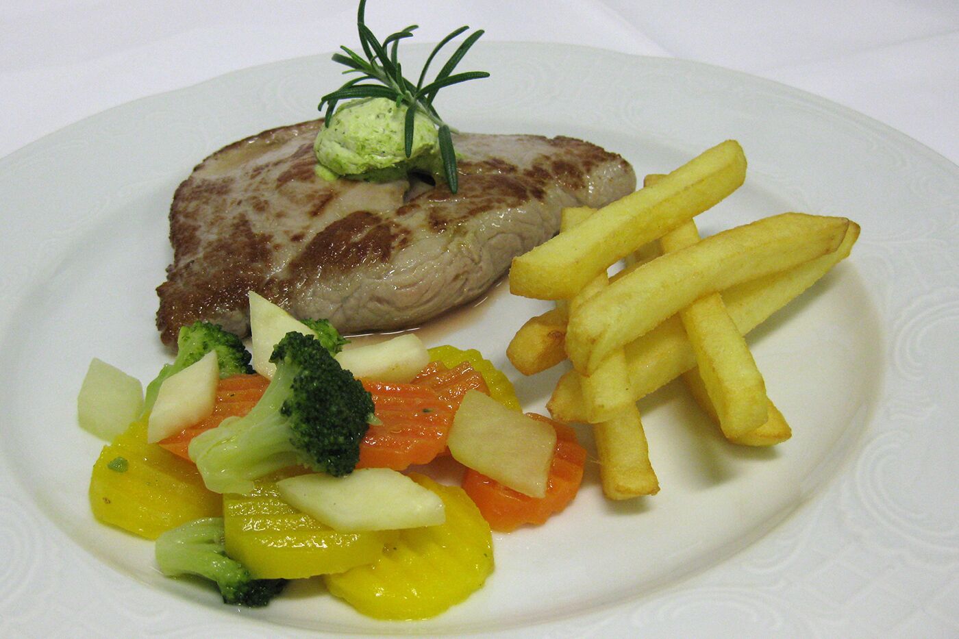 A plate with a grilled meat, French fries, and a side of mixed vegetables including broccoli and carrots.