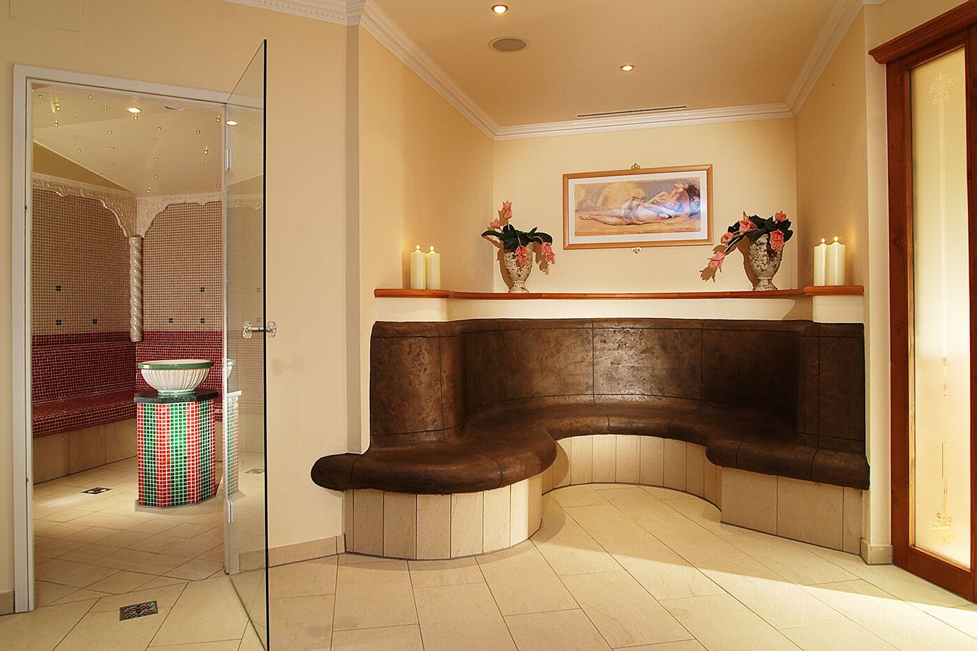 A corner seating area with a curved bench, a glass door leading to a room with a checkered bench, and a painting on the wall.