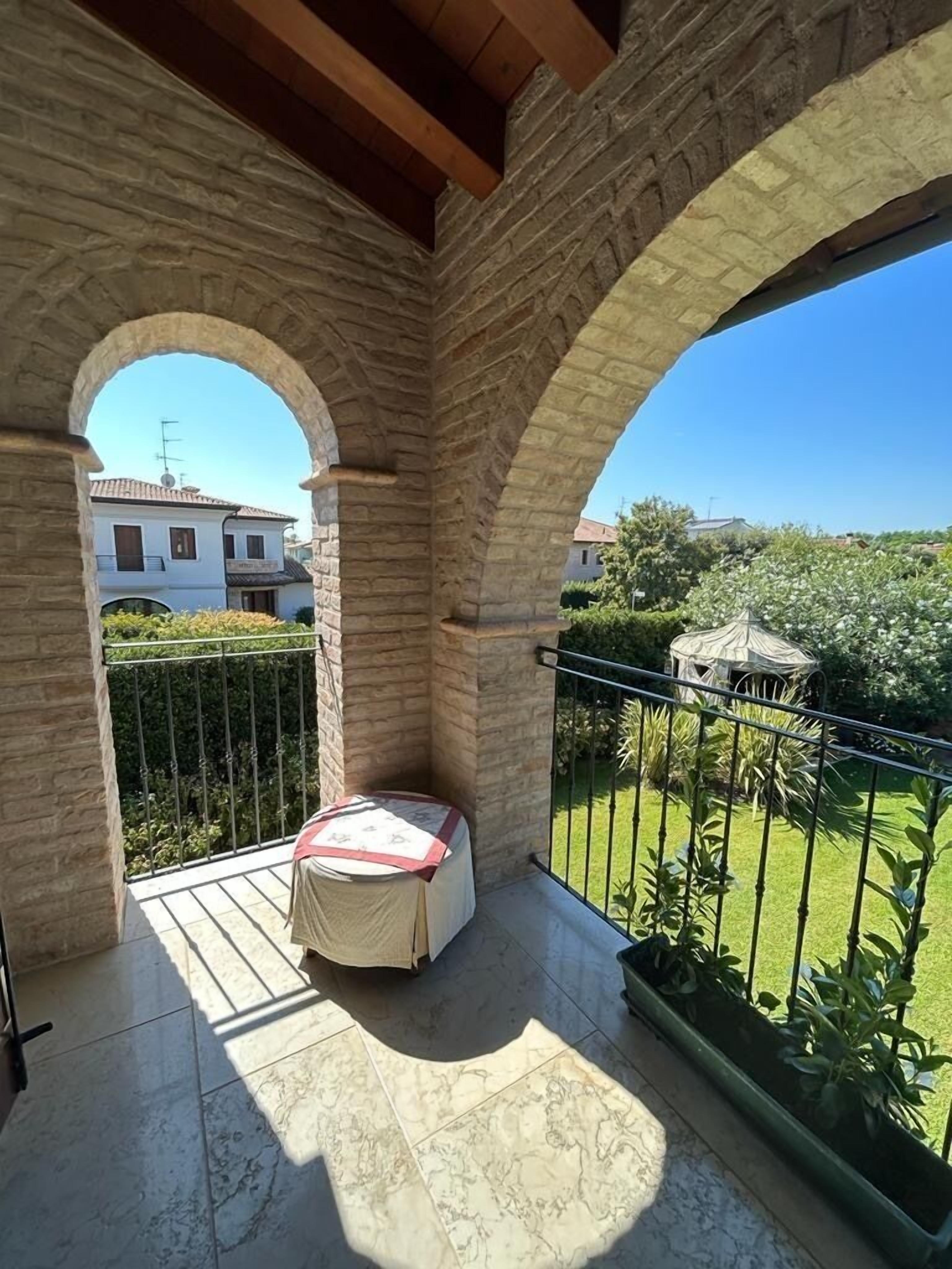 Un balcon doté d’un espace salon abrité, de murs en pierre et offrant une vue sur un jardin et des bâtiments.