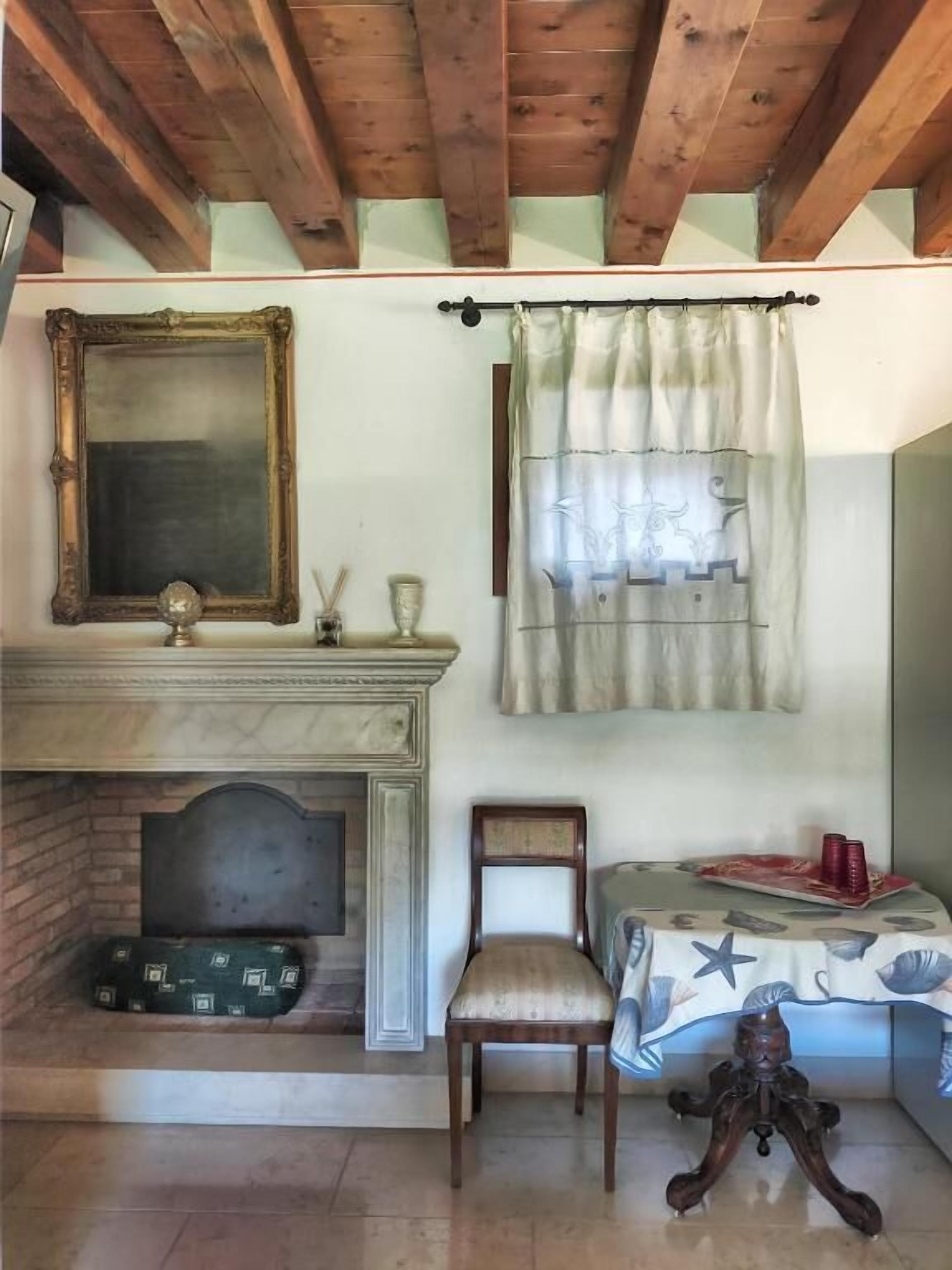 A room with a fireplace, a mirror, a chair, and a table with a tablecloth.