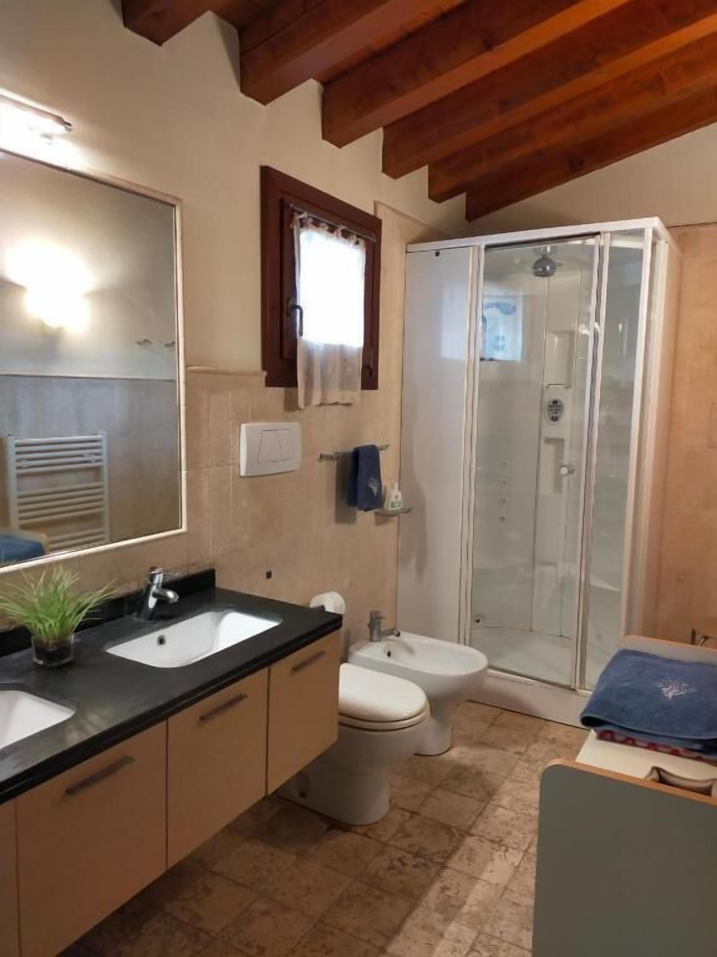 Un baño con un espejo grande, dos lavamanos, un bidé y una ducha con mampara de cristal.