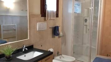 Un baño con un espejo grande, dos lavamanos, un bidé y una ducha con mampara de cristal.