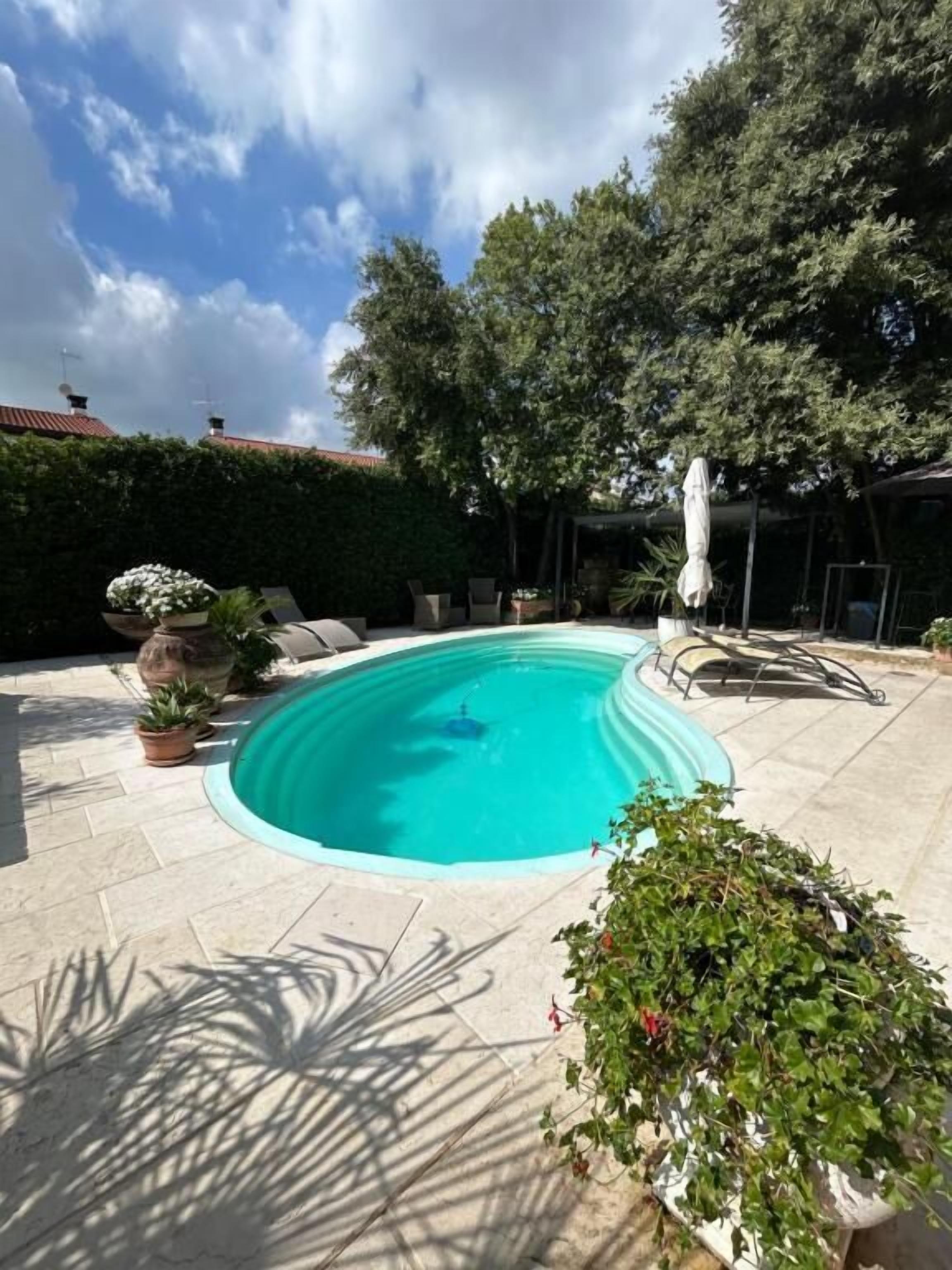 A swimming pool with a tiled deck, surrounded by potted plants and outdoor furniture.