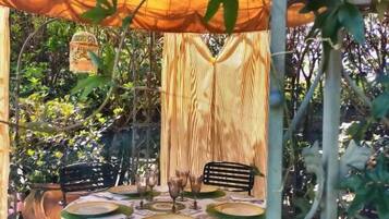 Un área de comedor al aire libre con una mesa dispuesta para cuatro personas, rodeada de sillas, bajo una marquesina.