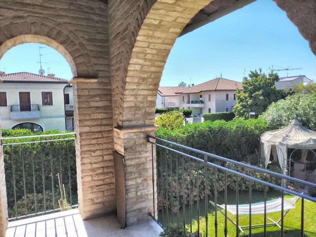 Un balcón con arcos de piedra, un jardín con quiosco y edificios residenciales al fondo.