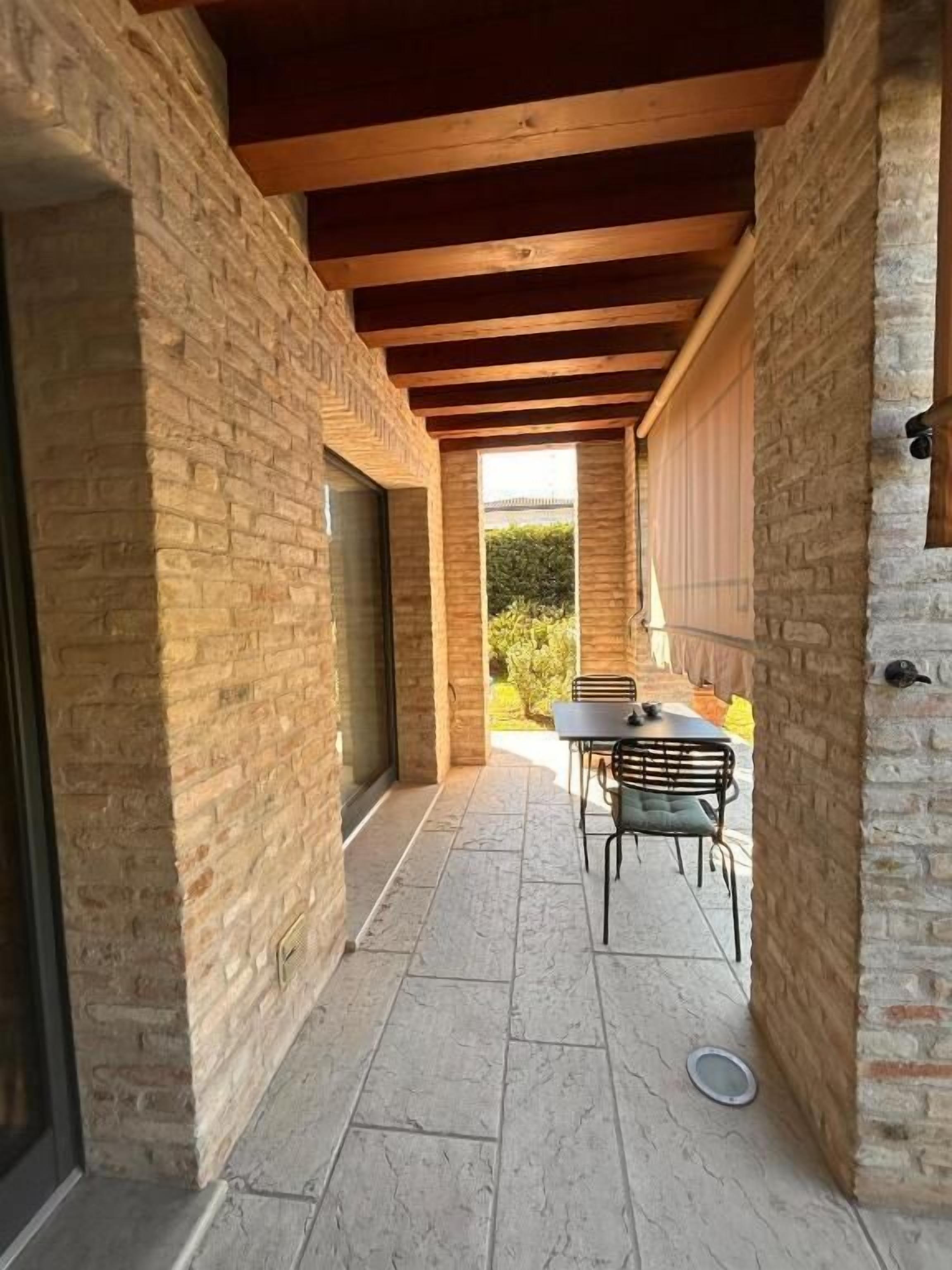 Un patio al aire libre cubierto con suelo de piedra, una mesa y sillas, y vistas a zonas verdes.
