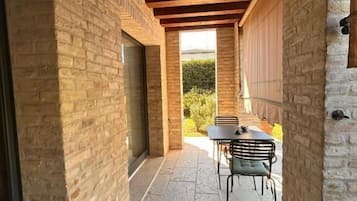 Un patio al aire libre cubierto con suelo de piedra, una mesa y sillas, y vistas a zonas verdes.