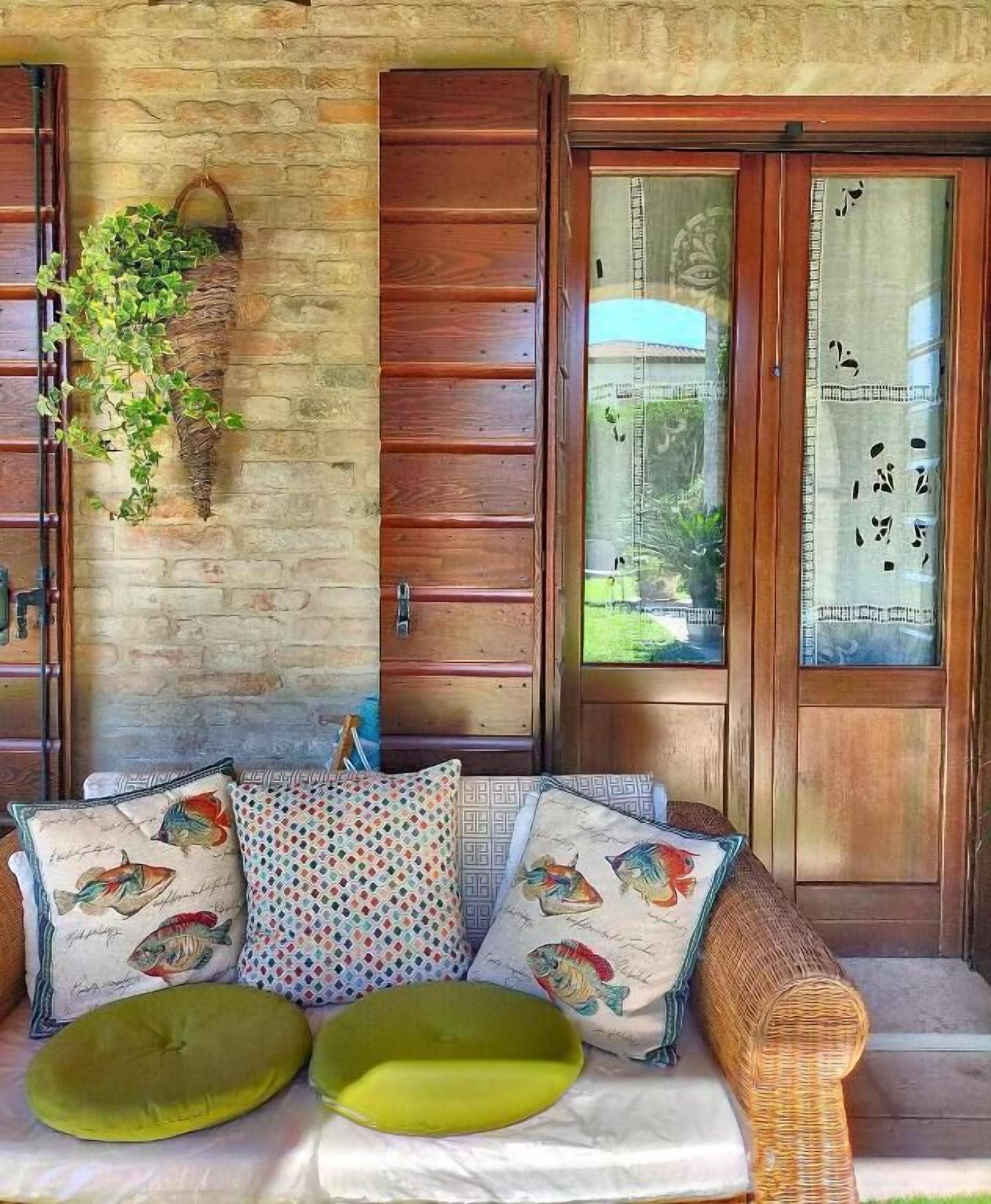 Un banco de madera con cojines, una planta colgante y una puerta de madera con ventanal.