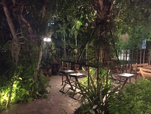 An outdoor garden area with stone flooring and wooden tables and chairs. - Buddy Guesthouse (Chiang Mai)