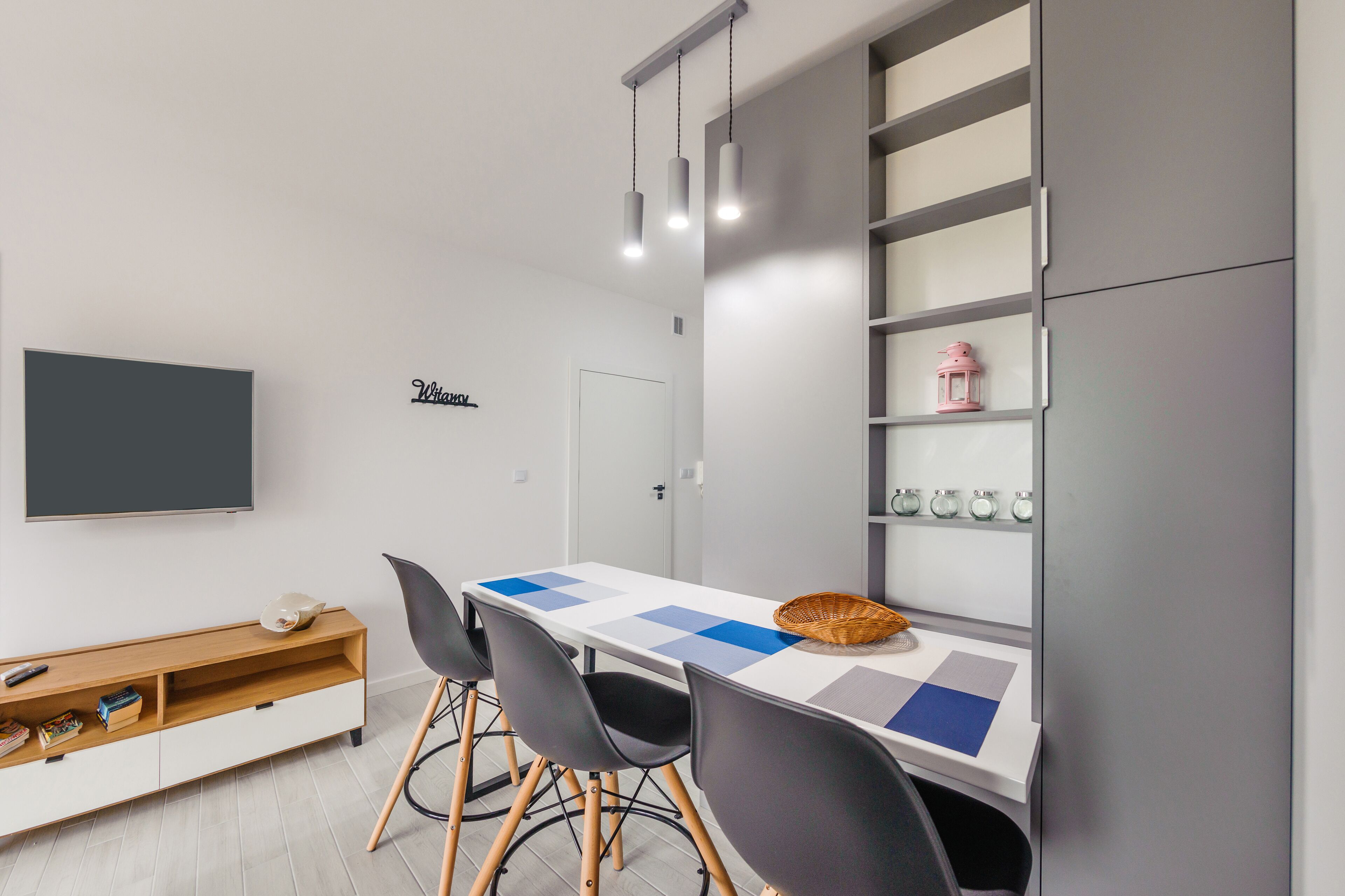 Un espace repas moderne avec une table blanche, des chaises noires et un meuble gris doté d’étagères.
