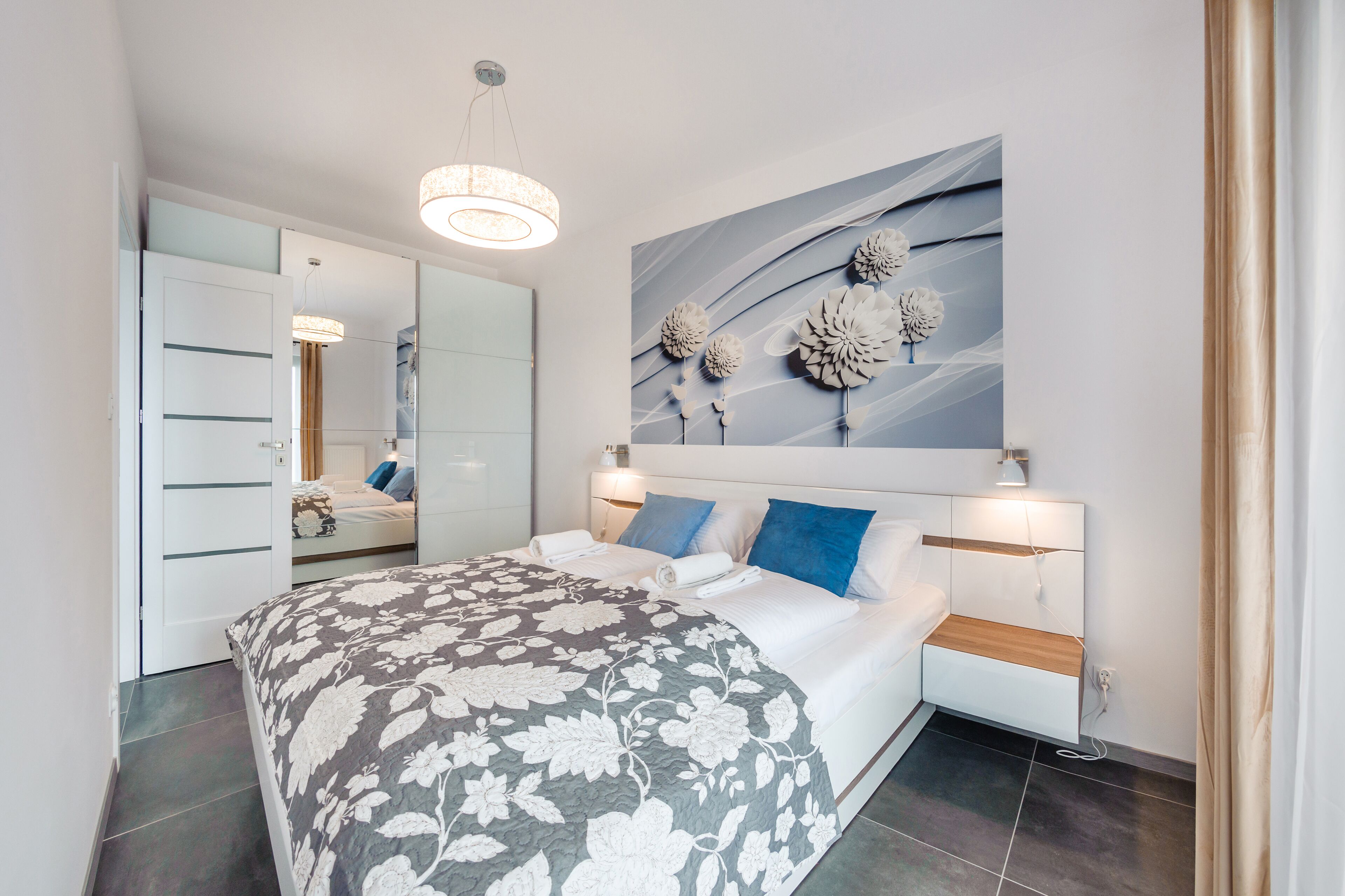 A modern bedroom with a large bed, a wall-mounted artwork, and a ceiling light.