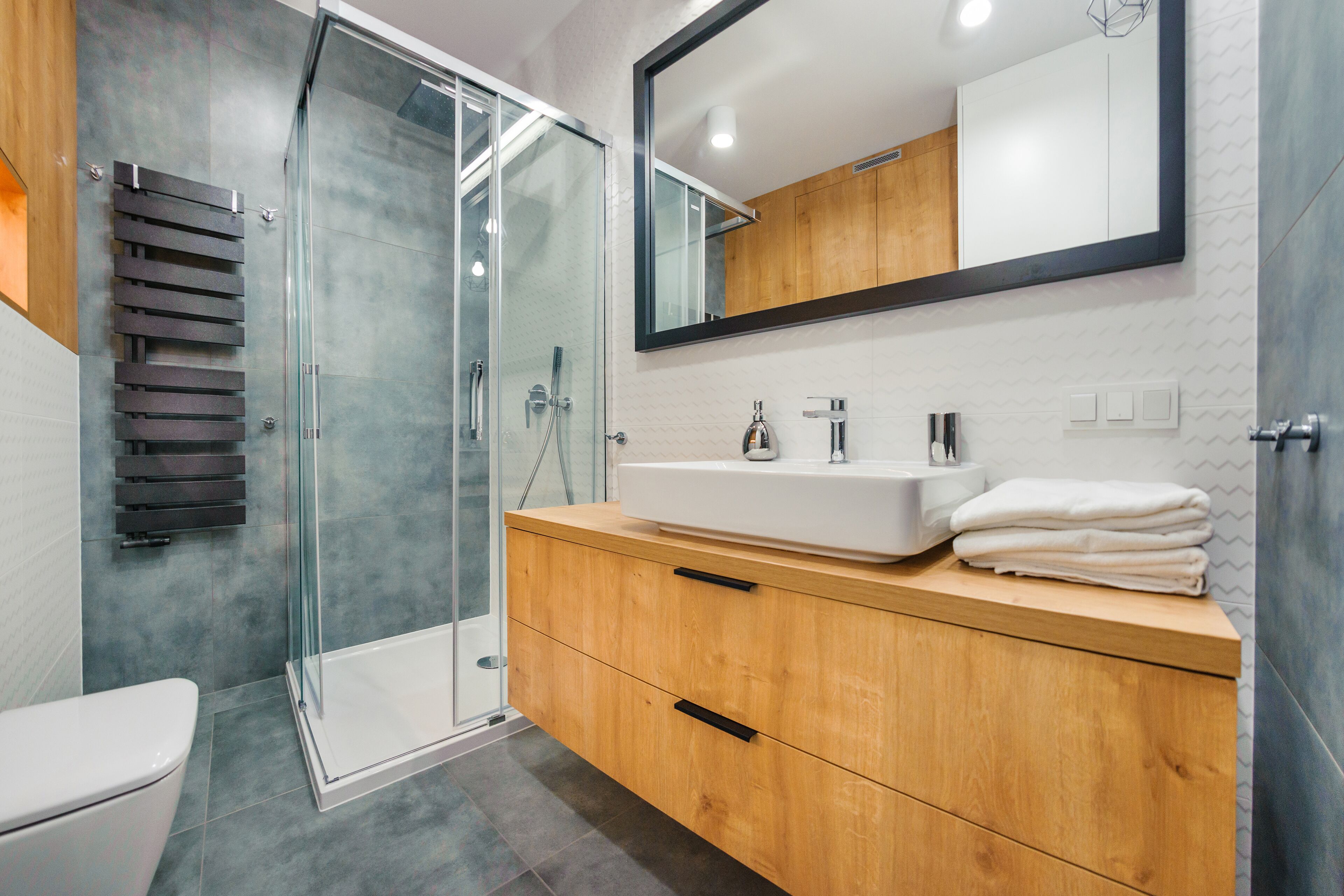 Une salle de bain moderne avec une douche à parois de verre, un meuble-lavabo en bois et un grand miroir au-dessus du meuble.
