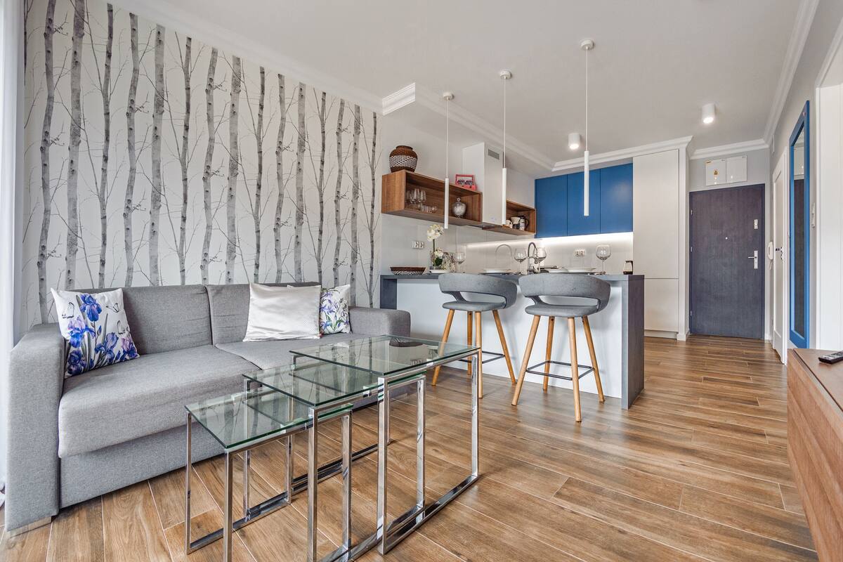 Een moderne woonkamer met een grijze bank, een glazen salontafel en een wand met een boommotief.