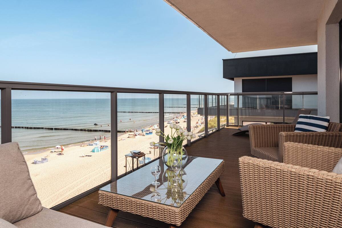 Een balkon met rieten meubilair, een glazen tafel en uitzicht op het strand.