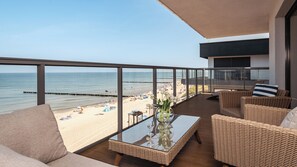 Een balkon met rieten meubilair, een glazen tafel en uitzicht op het strand.