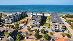 Un moderno complejo residencial con varias construcciones, una playa y una cancha de tenis.