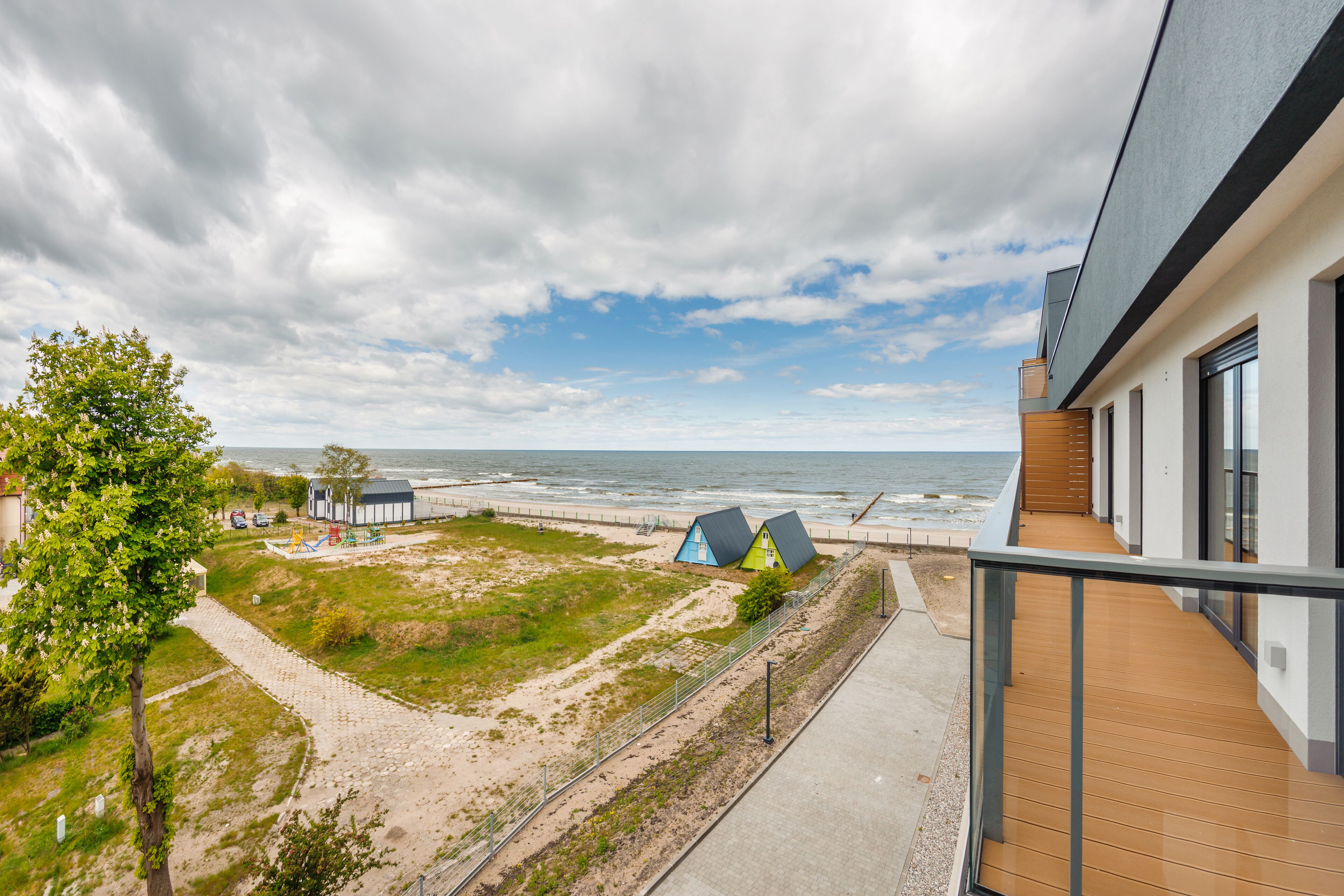 A coastal view from a balcony overlooking a sandy beach with a few buildings and a tree.