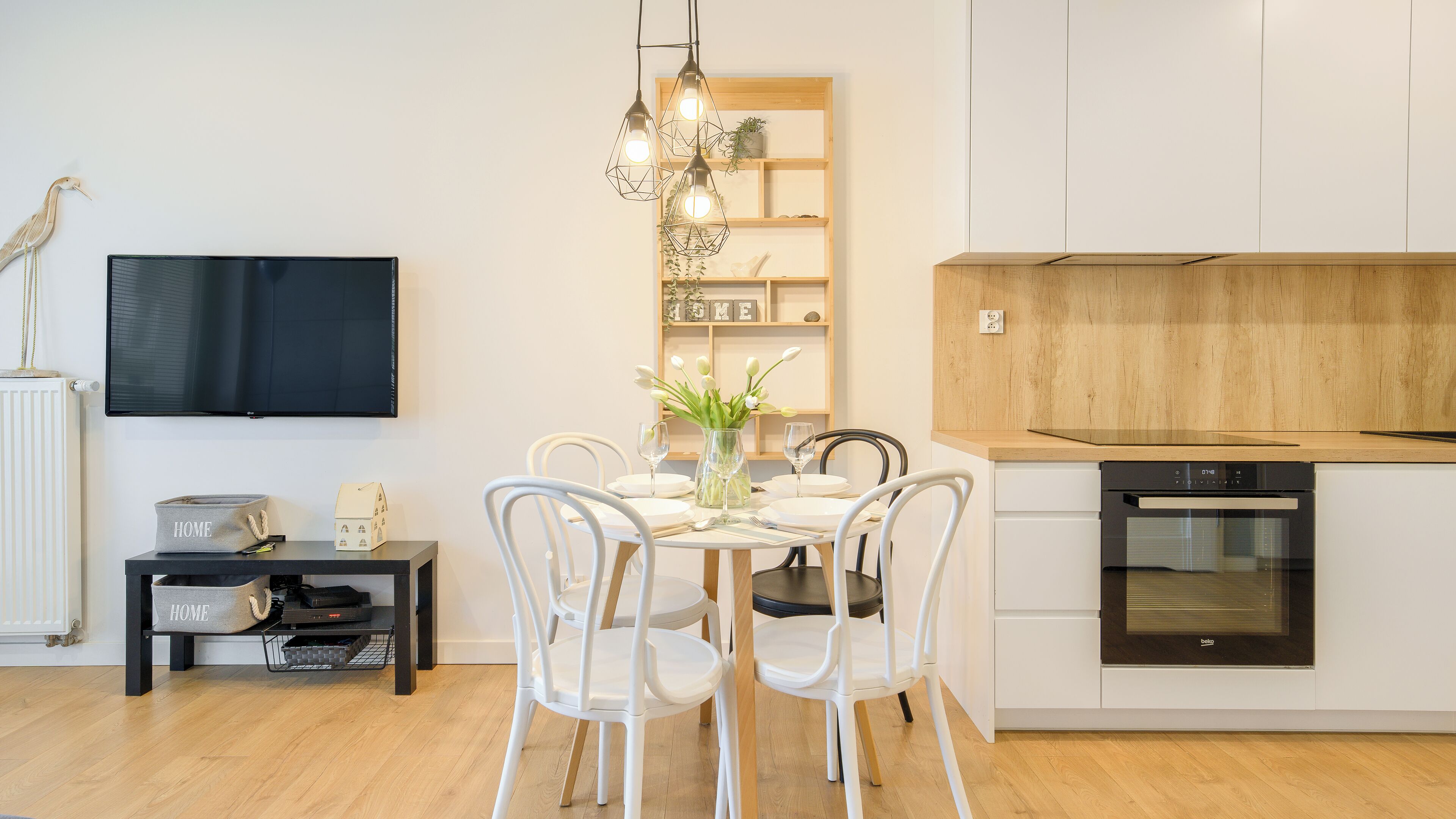 Une cuisine moderne avec des meubles blancs, un four encastré et un coin repas avec une table dressée pour deux personnes.