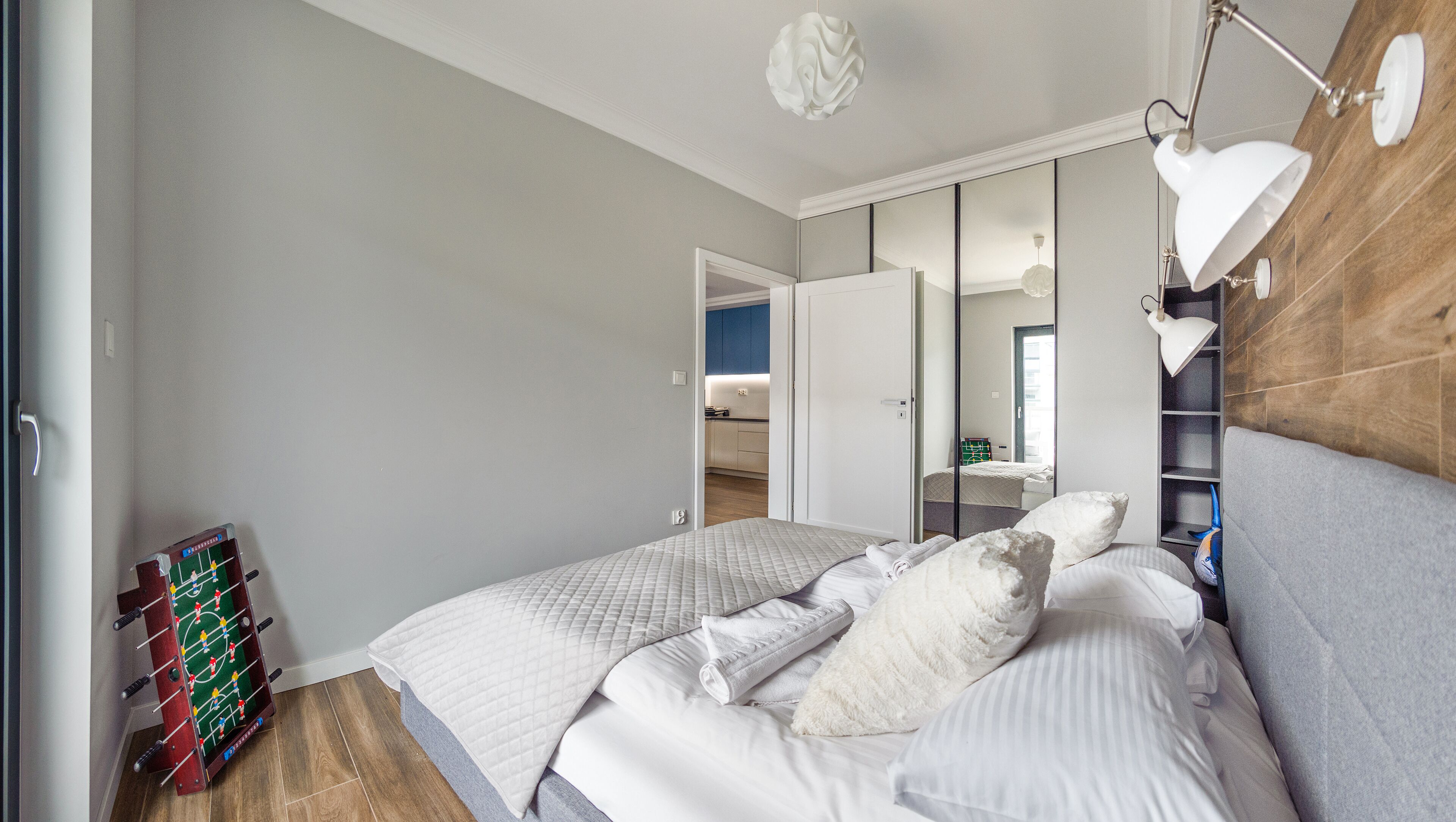 A bedroom with a bed, a bedside table, a mirror, and a wall-mounted lamp.