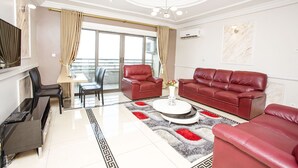 A modern living room with a red leather sofa set, a dining area with a table and chairs, and a balcony with curtains. - Résidence Le Carat Bonapriso (Douala)