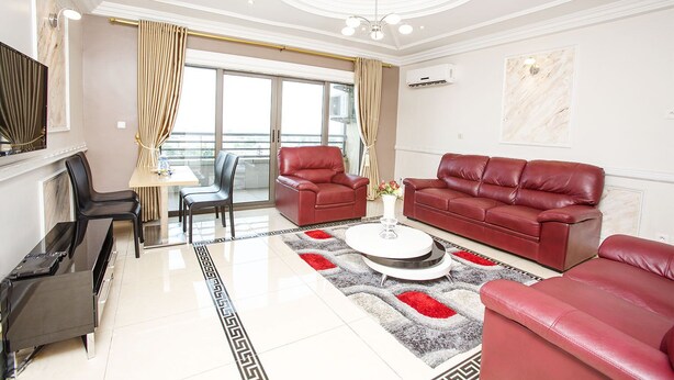 A modern living room with a red leather sofa set, a dining area with a table and chairs, and a balcony with curtains. - Résidence Le Carat Bonapriso (Douala)