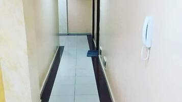 Un couloir aux murs et au sol recouverts de carreaux blancs, un symbole encadré sur le mur et un appareil blanc fixé au mur, sur la droite.