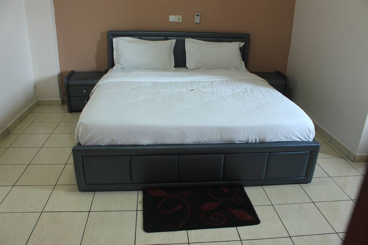 A neatly made bed with white linens, a dark headboard, and a small bedside table with a lamp.