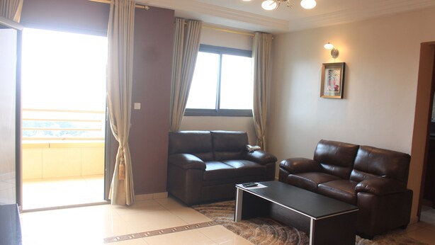 A living room with two brown leather sofas, a coffee table, and a large window with curtains. - Résidence Le Carat Bonapriso (Douala)