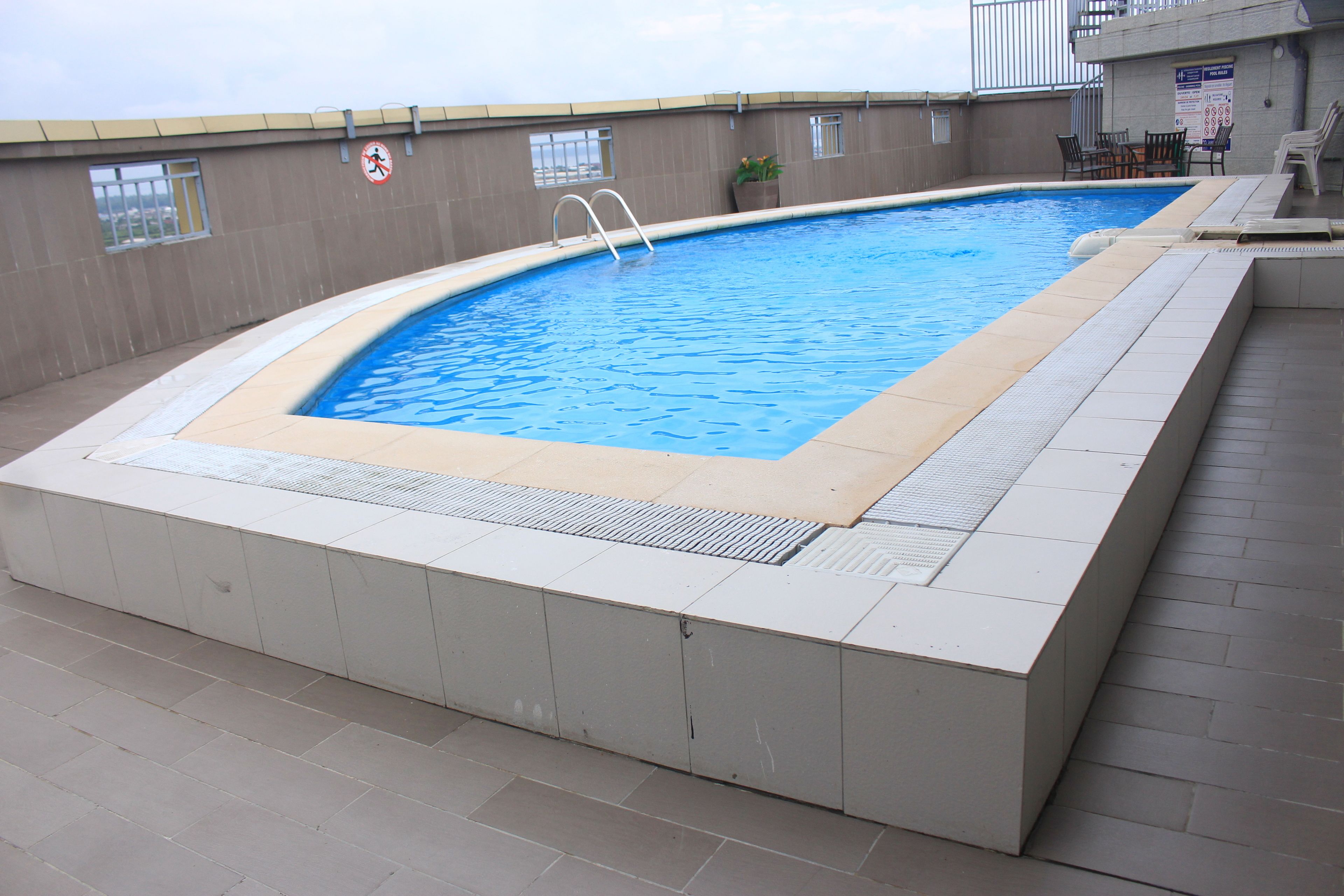 Une piscine intérieure rectangulaire, bordée de carreaux, avec une échelle et un panneau indiquant qu’il est interdit de se baigner.