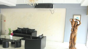A modern living room with a glass coffee table, black sofas, and a decorative statue. - Résidence Le Carat Bonapriso (Douala)