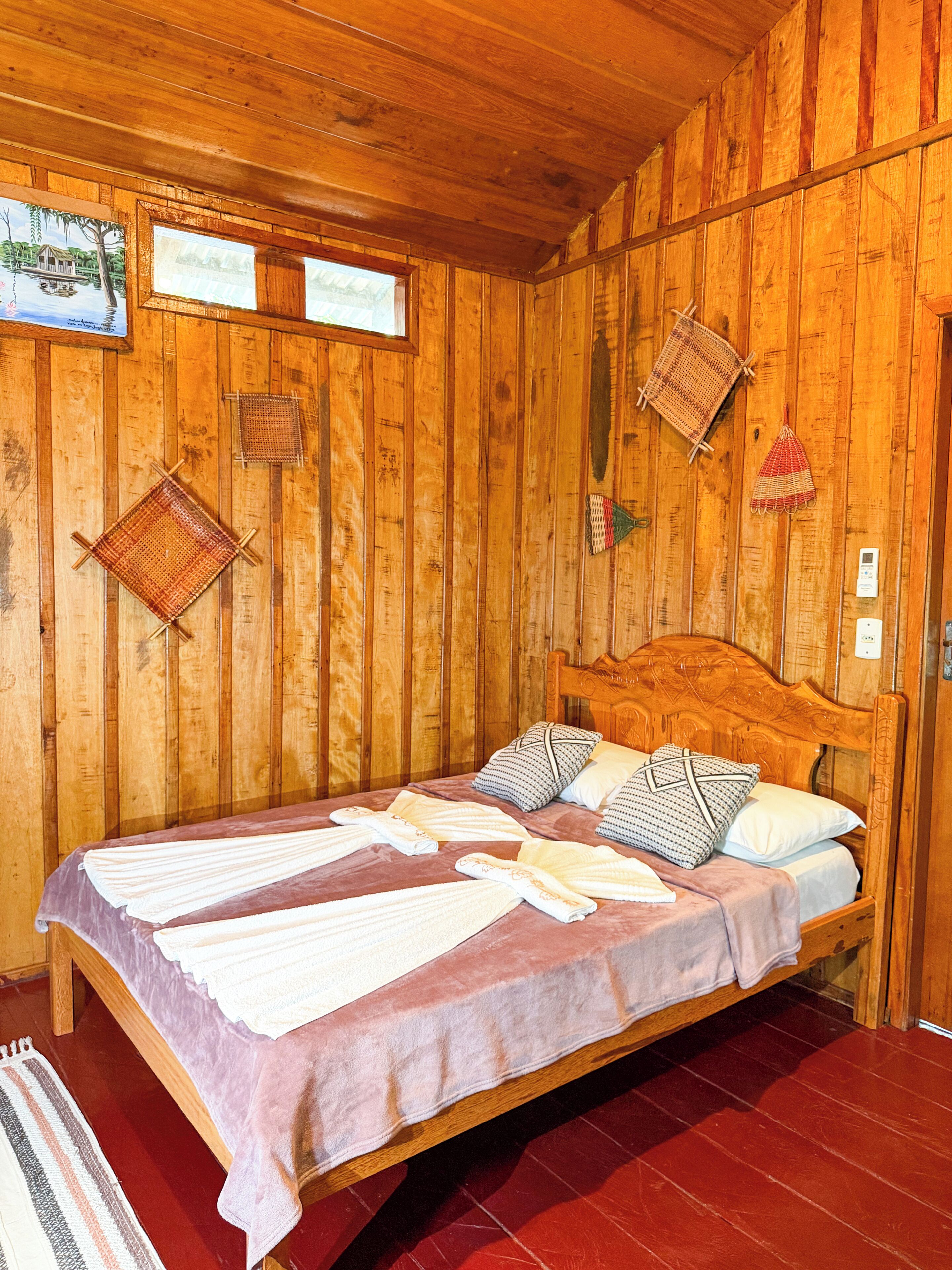 A wooden room with a bed, wooden walls, and a red floor.