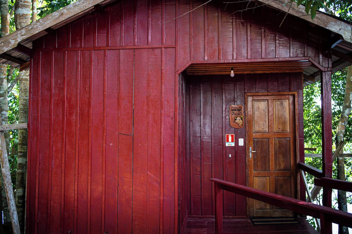 Une cabane en bois rouge, avec une porte en bois, un petit porche et une enseigne au-dessus de la porte.