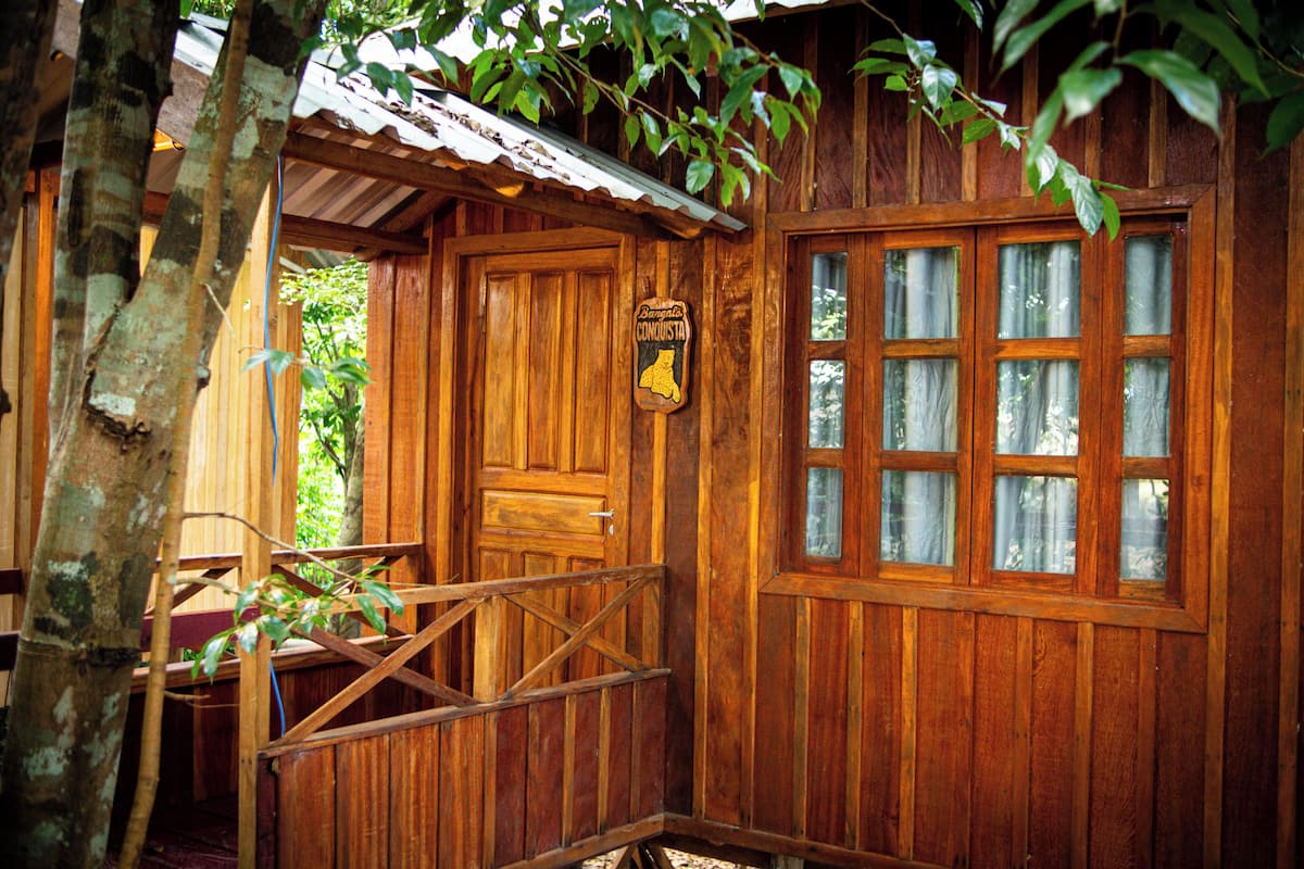 Une cabane en bois avec une porte en bois, une fenêtre avec des rideaux et une enseigne au-dessus de la porte.