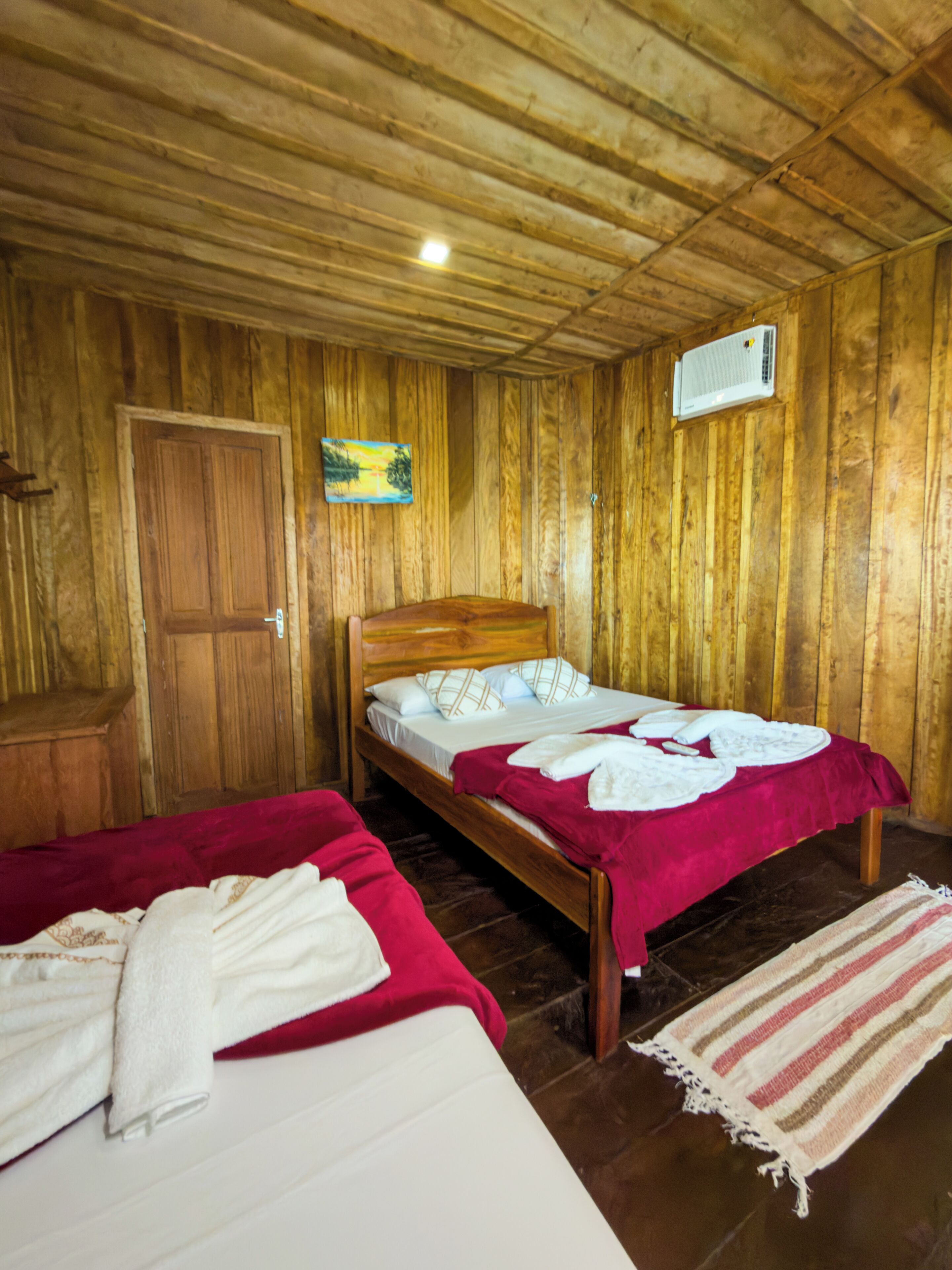 A wooden room with two beds, a door, and a wall-mounted air conditioner.