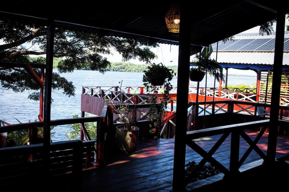 Une terrasse en bois offrant une vue sur un lac, un espace salon couvert et un bâtiment avec un toit rouge.