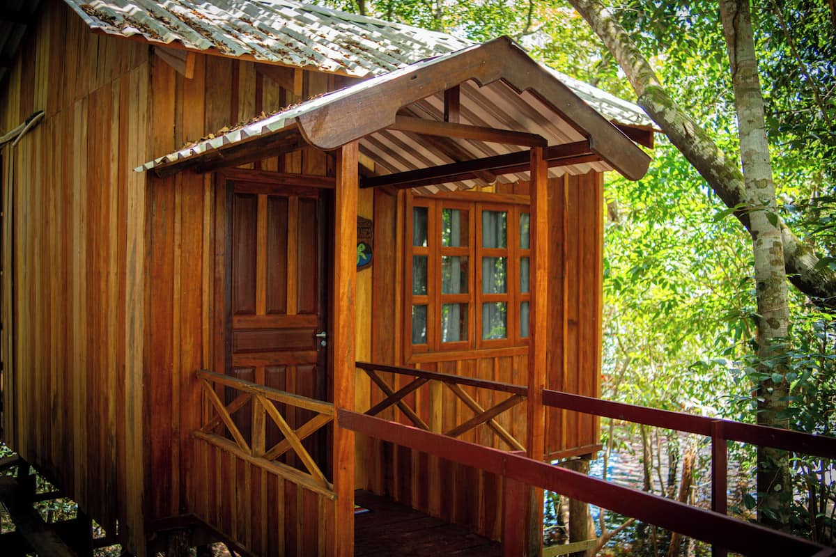Une cabane en bois dotée d’un porche, d’une porte avec des panneaux de verre et d’un toit en métal.