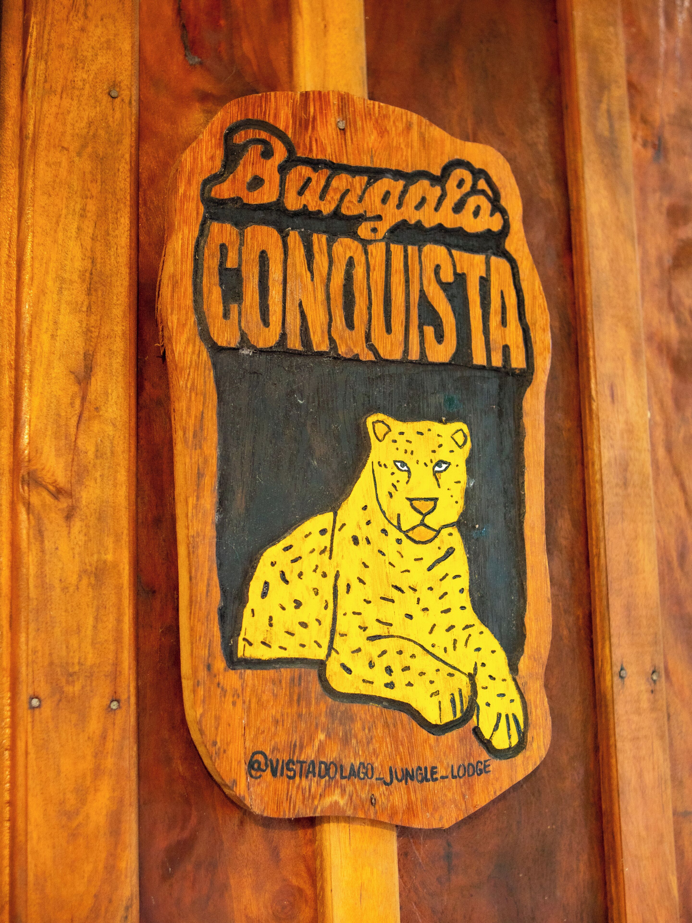 Ein Holzschild mit dem Schriftzug 'Bangalo Conquista' und einer Illustration einer Leoparden-Abbildung.