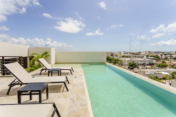 A rooftop infinity pool with lounge chairs and a clear view of the cityscape.