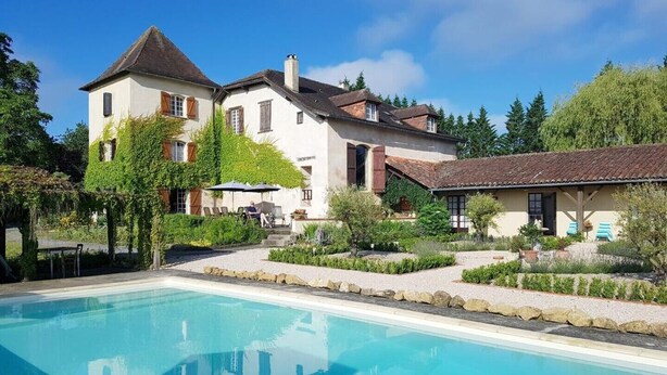 Una casa grande con piscina, rodeada de follaje y un cielo despejado.
