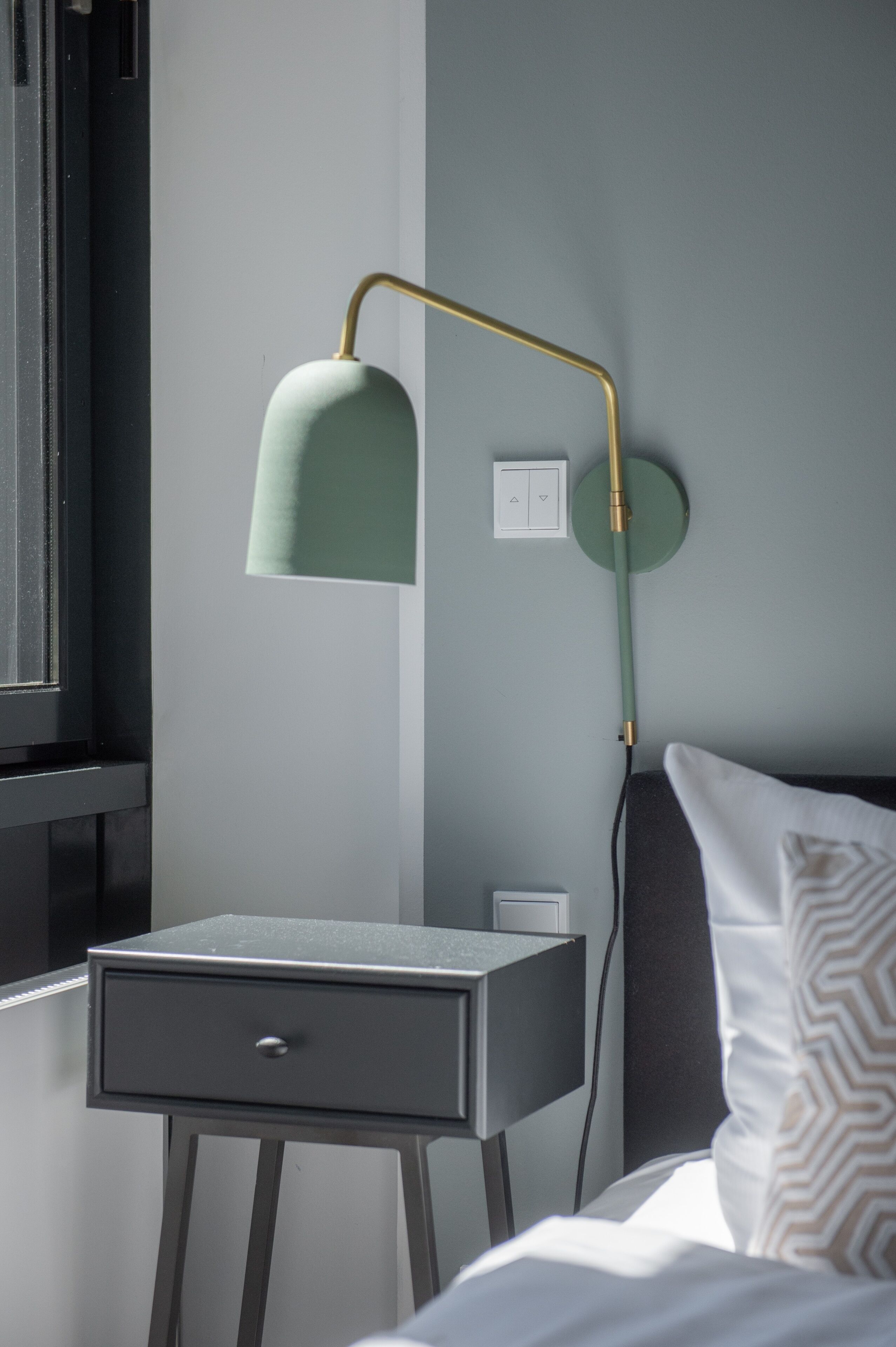 A bedside table with a lamp, a power outlet, and a switch on the wall.
