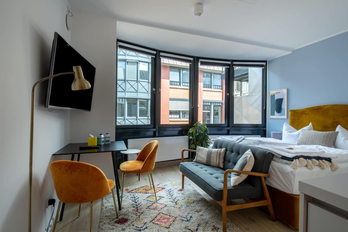 Una habitación de hotel moderna con un ventanal grande, una cama, un escritorio, una silla y un sofá.