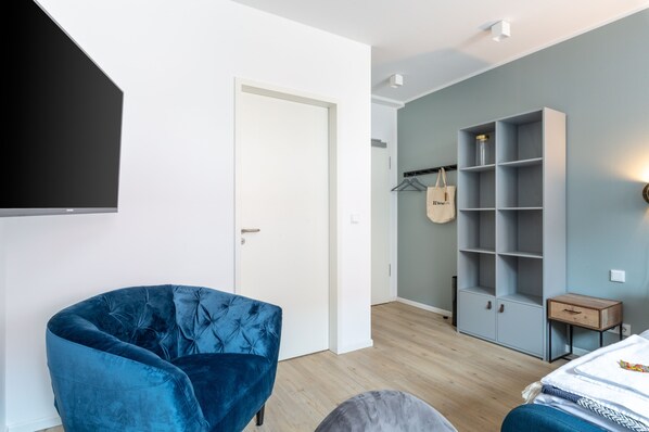 Un dormitorio moderno con un sillón de terciopelo azul, un armario gris y una cama con una colcha estampada.