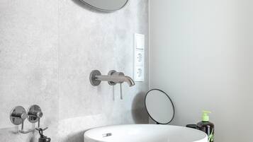 Un baño con lavamanos blanco, un espejo redondo, un cabezal de ducha de mano y un secador de pelo de mano.