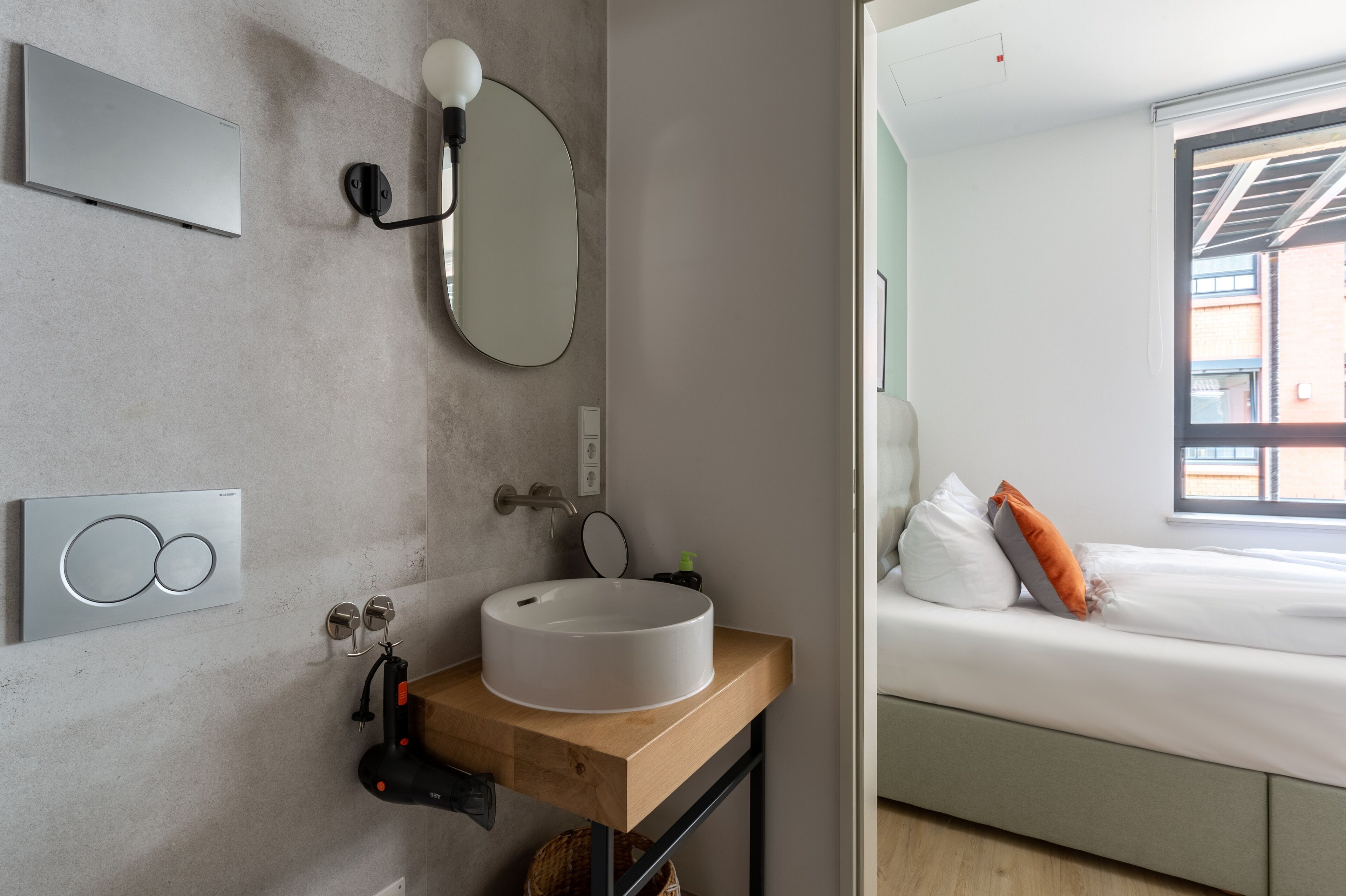 A modern bathroom with a round sink, a large mirror, and a wall-mounted light fixture.