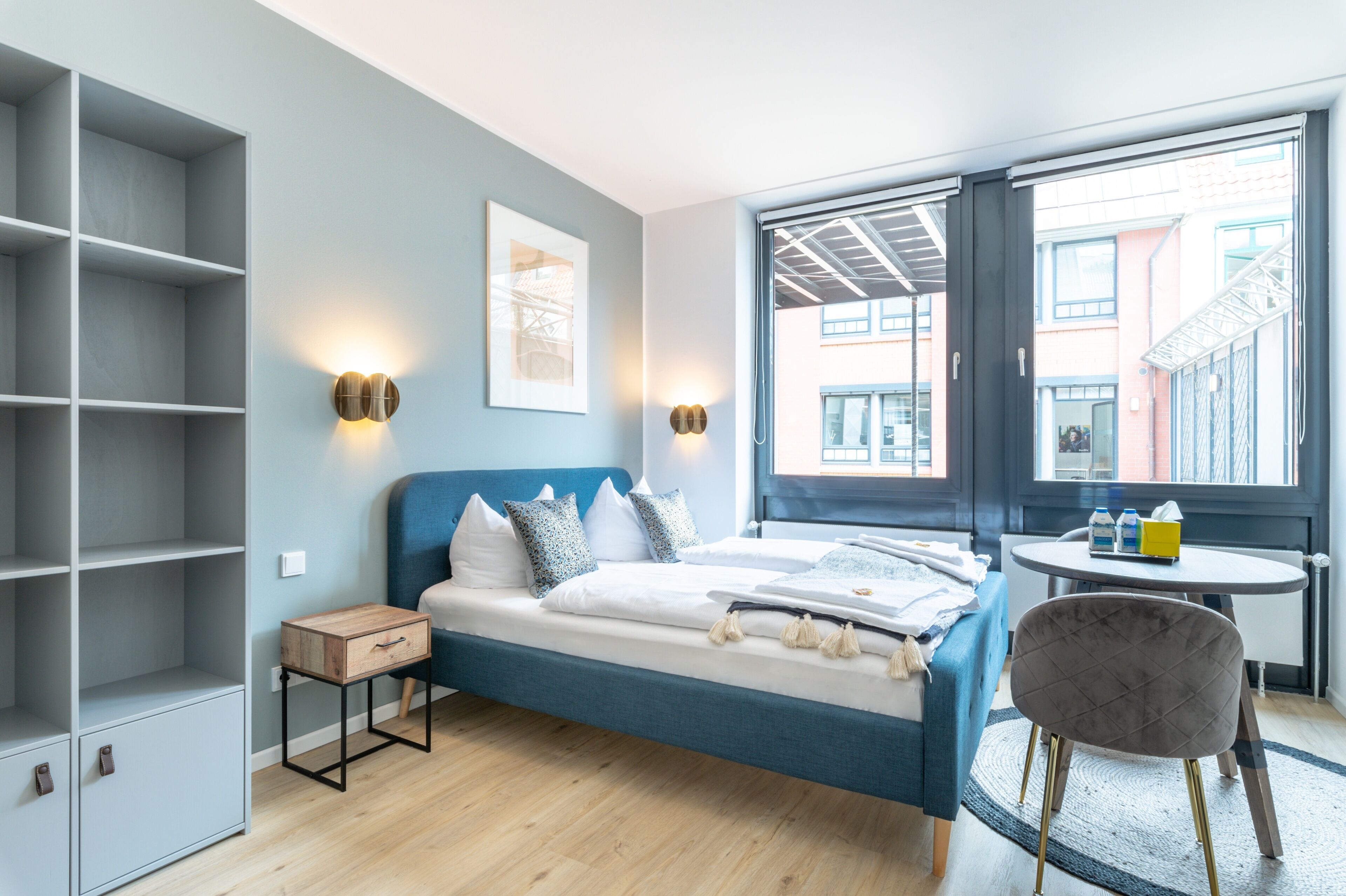 Une chambre à coucher moderne, avec un lit, des tables de chevet, une chaise, une fenêtre et une vue sur les bâtiments environnants.