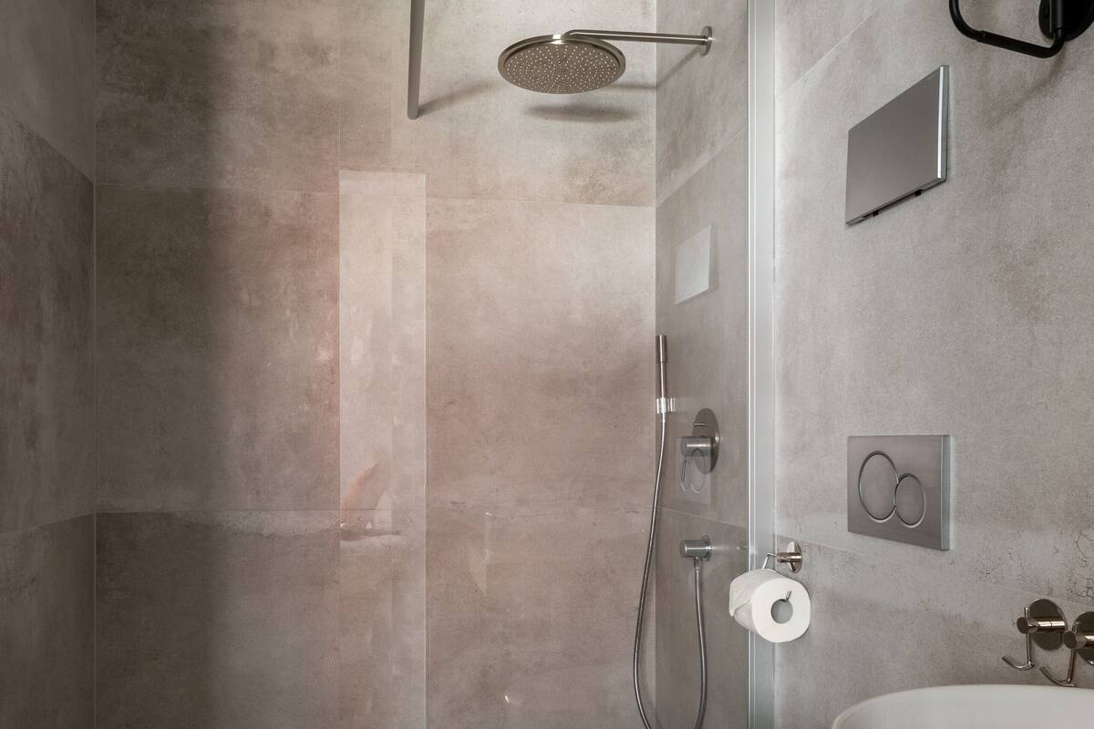 Un baño moderno con ducha envuelta en vidrio, inodoro blanco y tocador de madera con lavamanos grande.