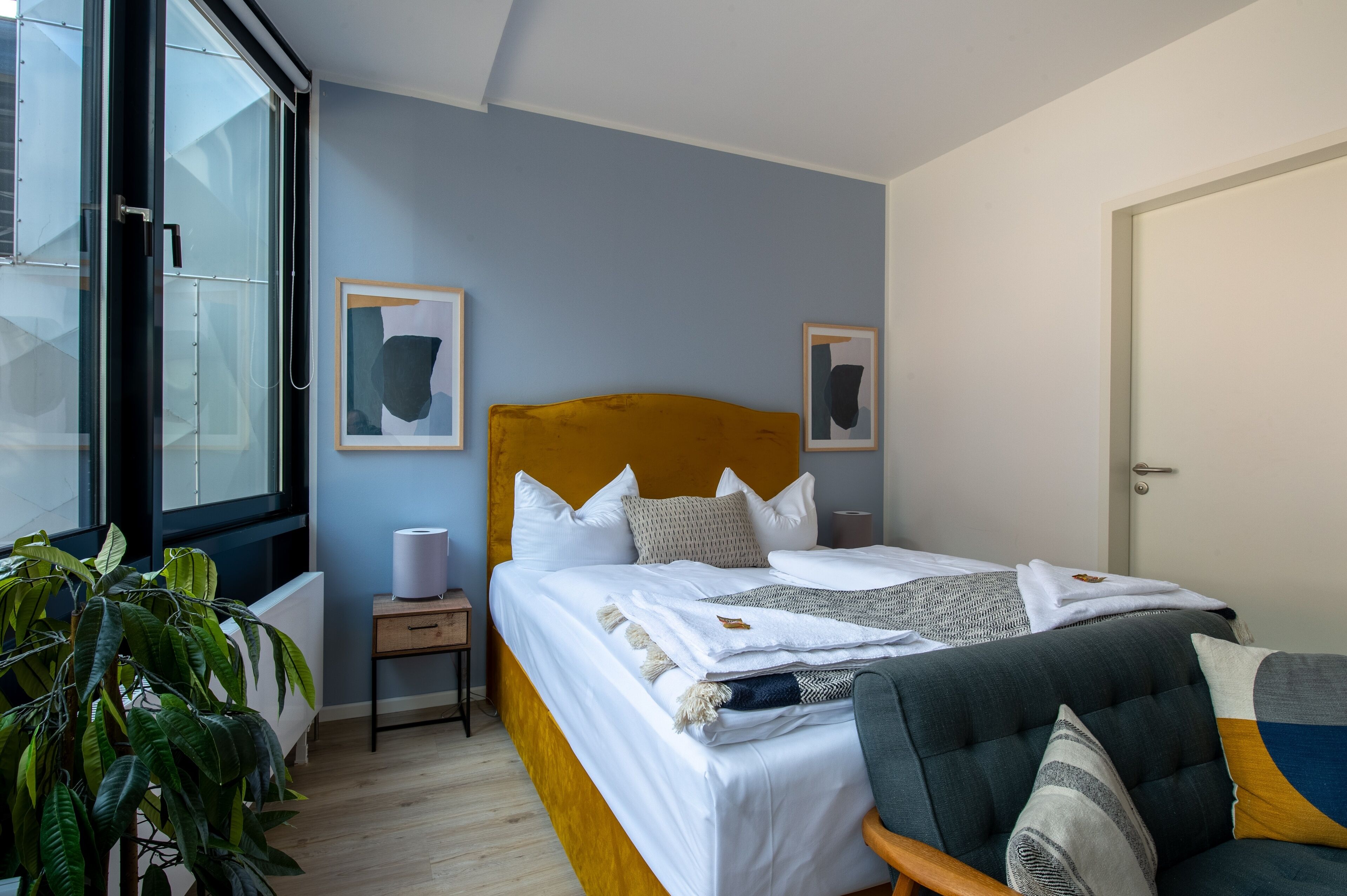 Un dormitorio con cama, mesita de noche, silla y un ventanal grande.