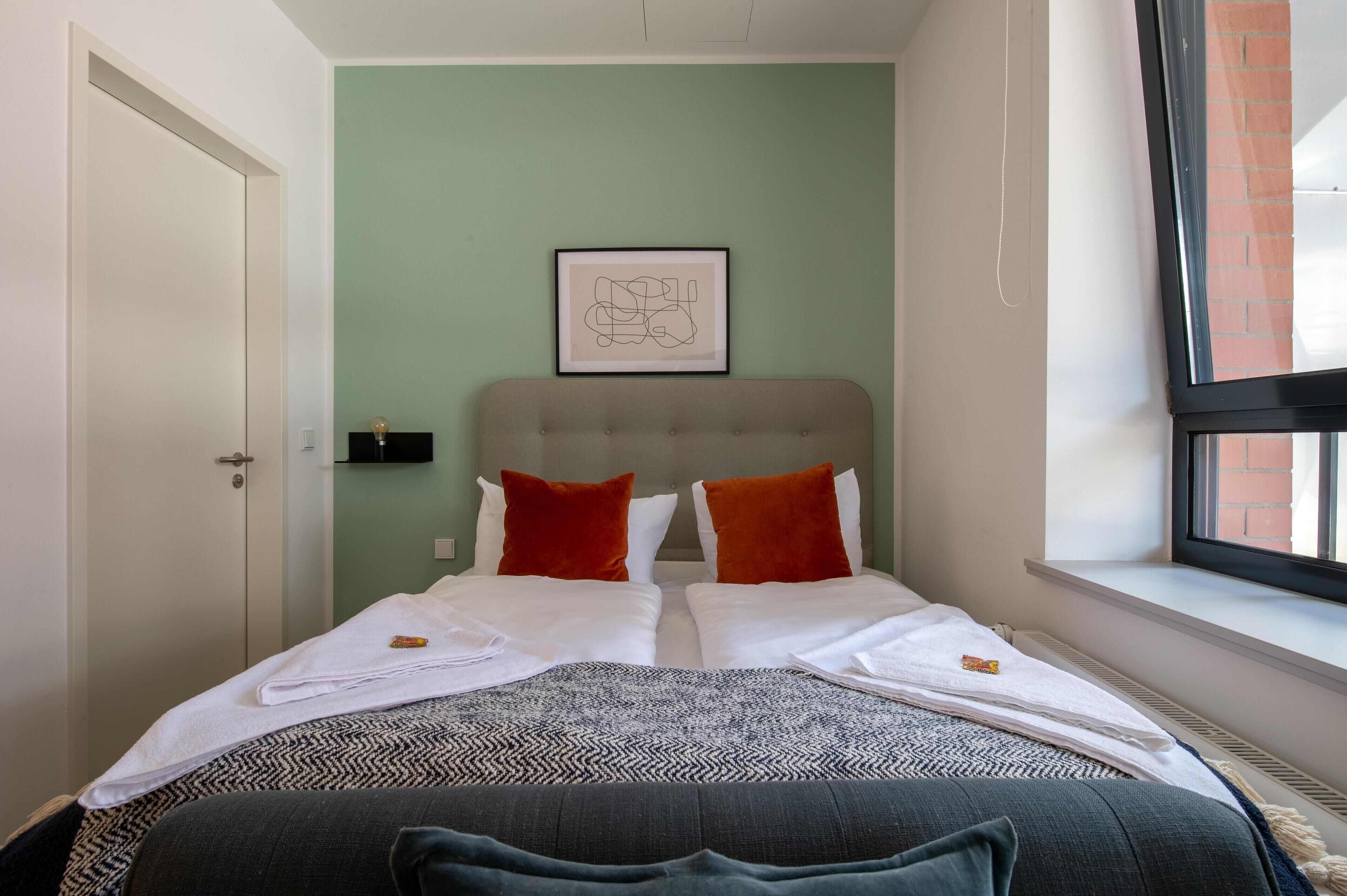 A double bed with white linens, two red pillows, and a grey headboard. A framed abstract artwork hangs above the bed.